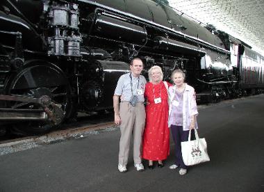 Three anniversary attendees standing beside a historic locomotive